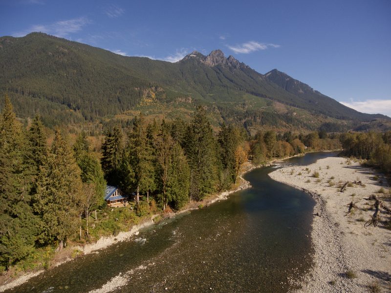 Aerial view of the chalet among trees beside the Skykomish River with Mount Baring behind