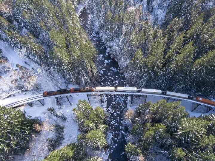 Aerial view of a freight train curving through snowy forest beside the Foss River