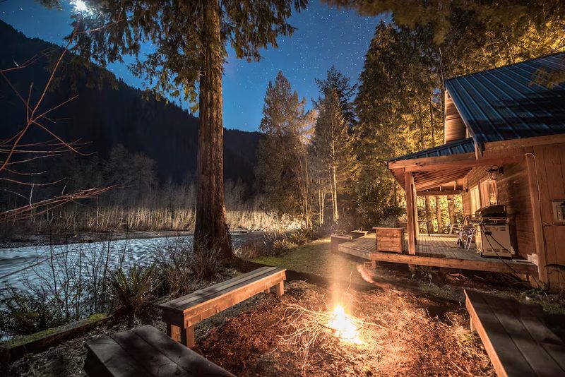 Fire pit burning beside the cabin at dusk with mountains beyond