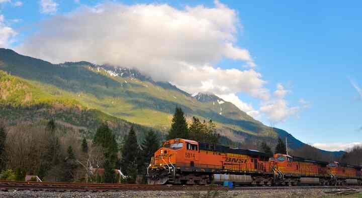 An orange BNSF freight train passing below the mountain